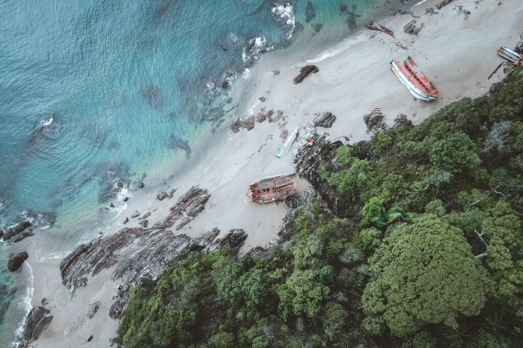 Aerial view of shipwrecks on a serene Chukai beach with lush greenery and rocky coastline.
